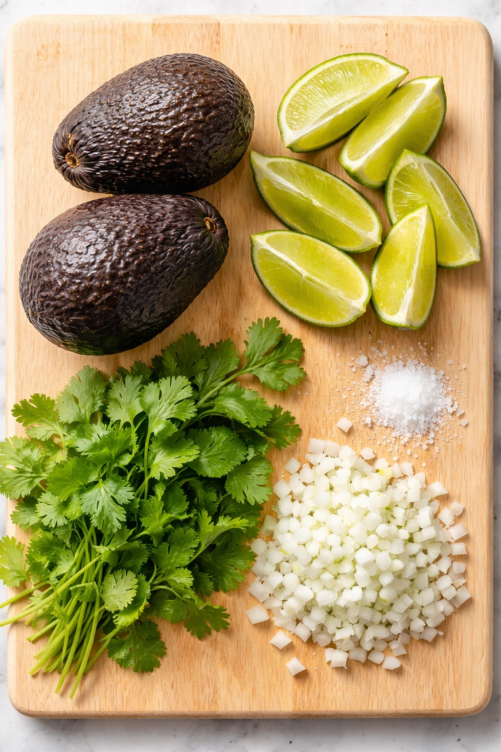 Top-down view of essential guacamole ingredients: avocados, limes, cilantro, onion, and salt