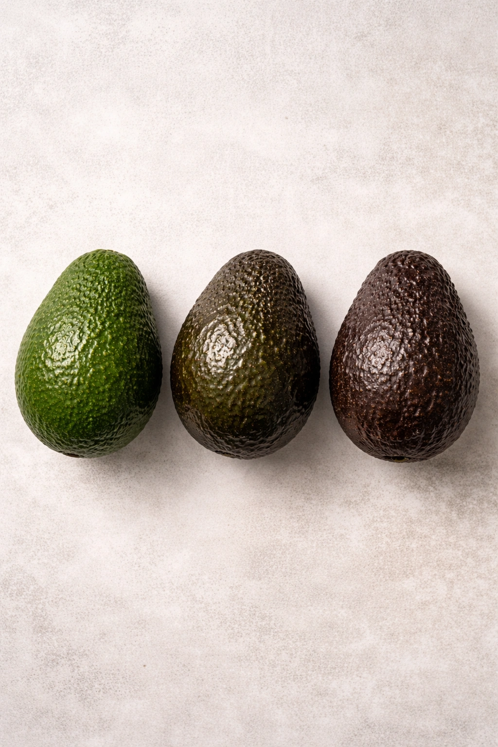 Three Hass avocados showing different ripeness levels