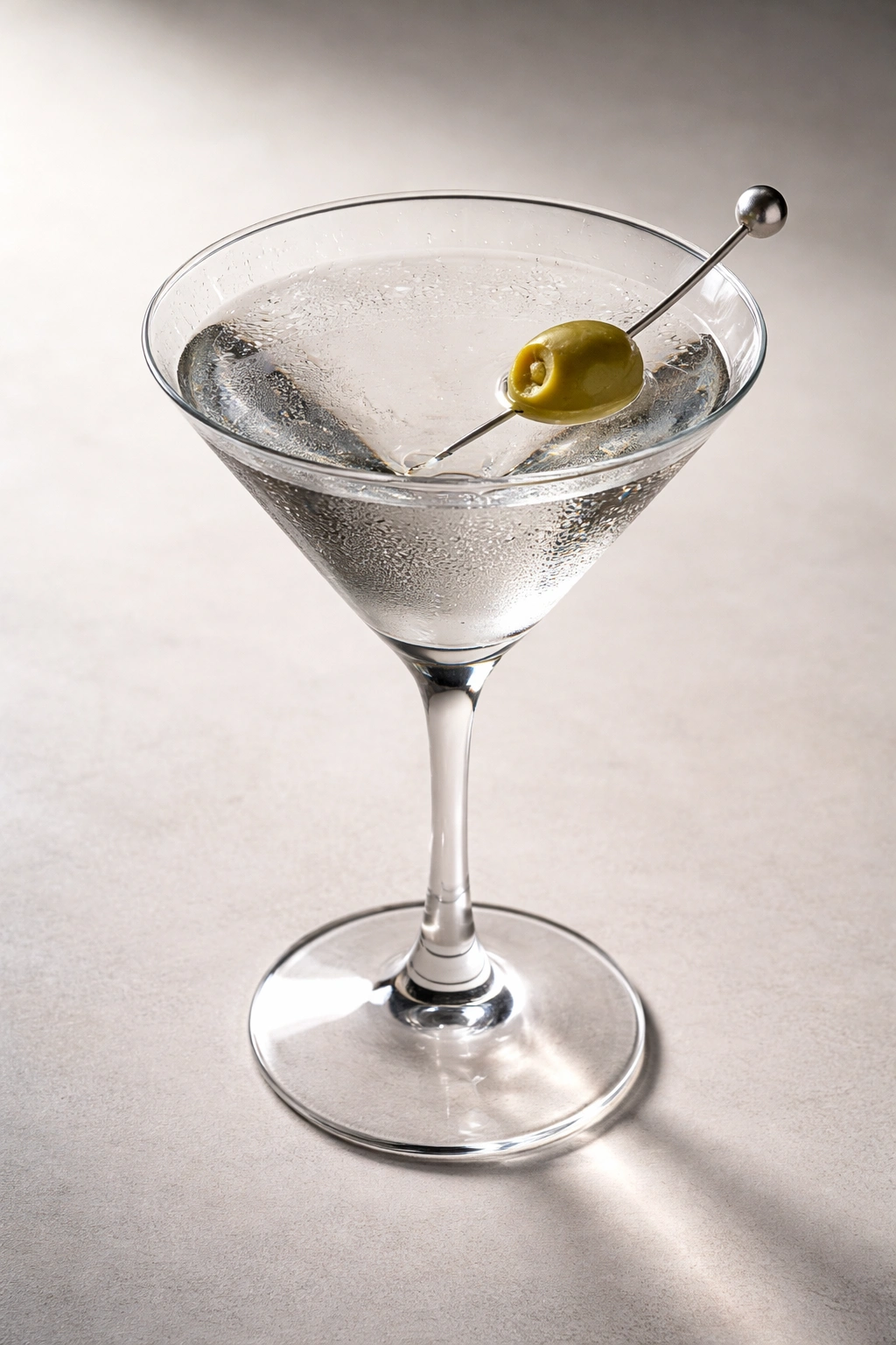 Close-up of a classic vodka martini with a green olive in a pristine glass.