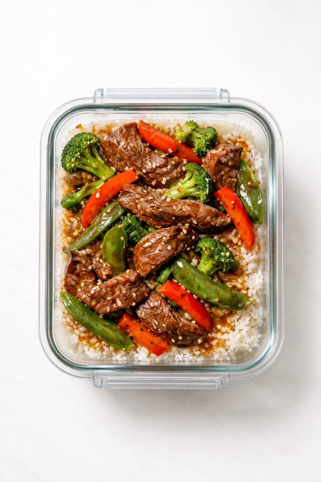 Airtight glass container of steak stir-fry with rice leftovers on a plain surface