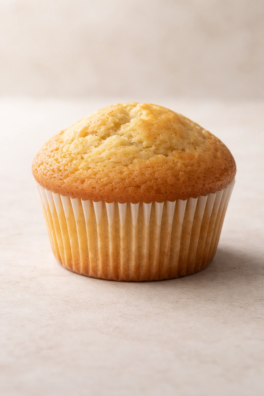 Close-up of a single golden muffin with a tender crumb on a neutral background