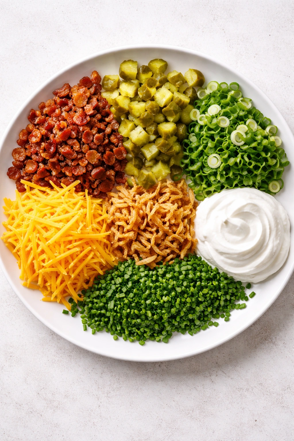 Plate of assorted toppings for cheeseburger soup: bacon, pickles, onions, cheddar, onions, sour cream, chives