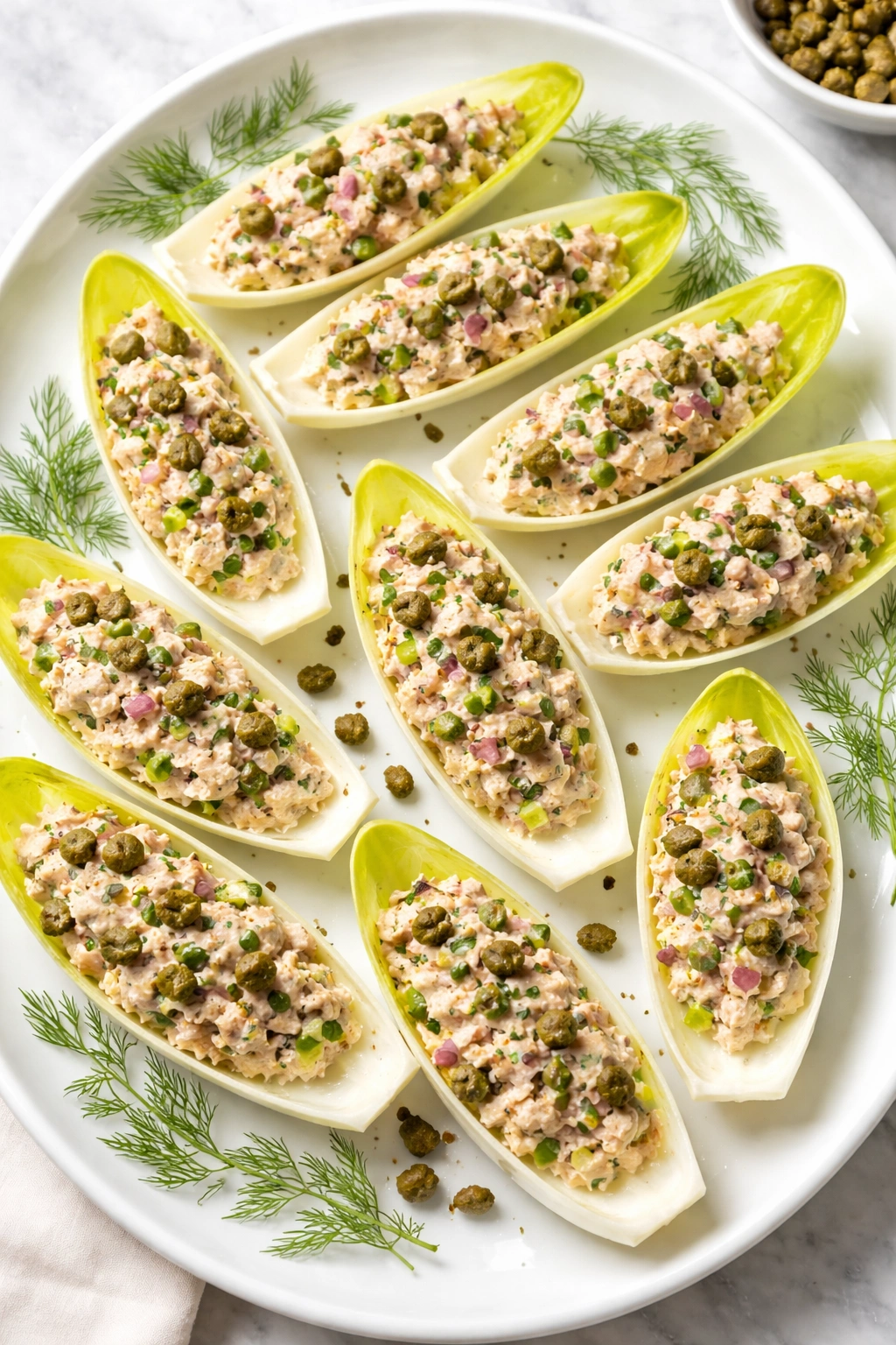 Endive boats filled with tuna salad and capers on a platter
