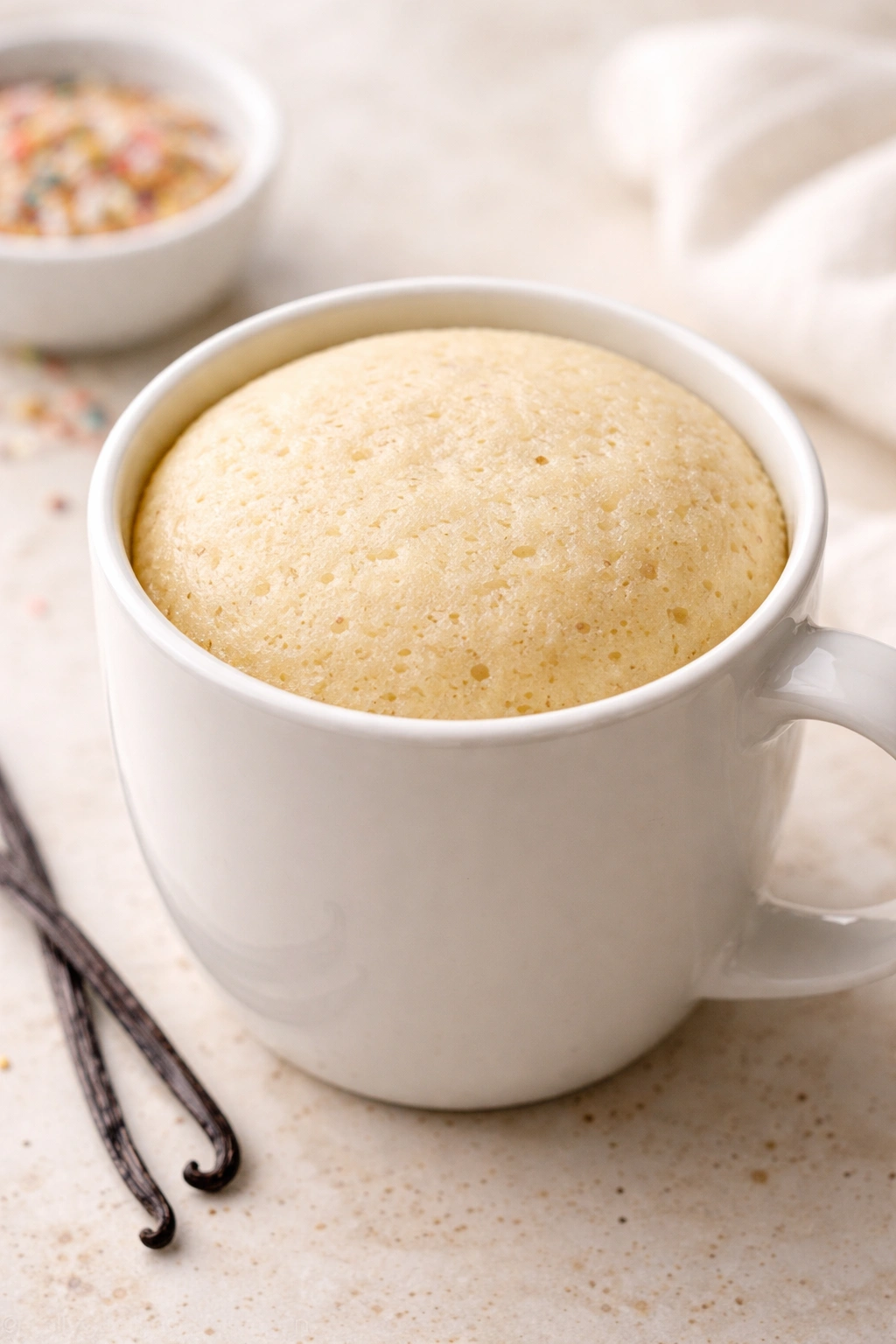 Close-up of a pale vanilla mug cake in a light mug on a soft-lit counter