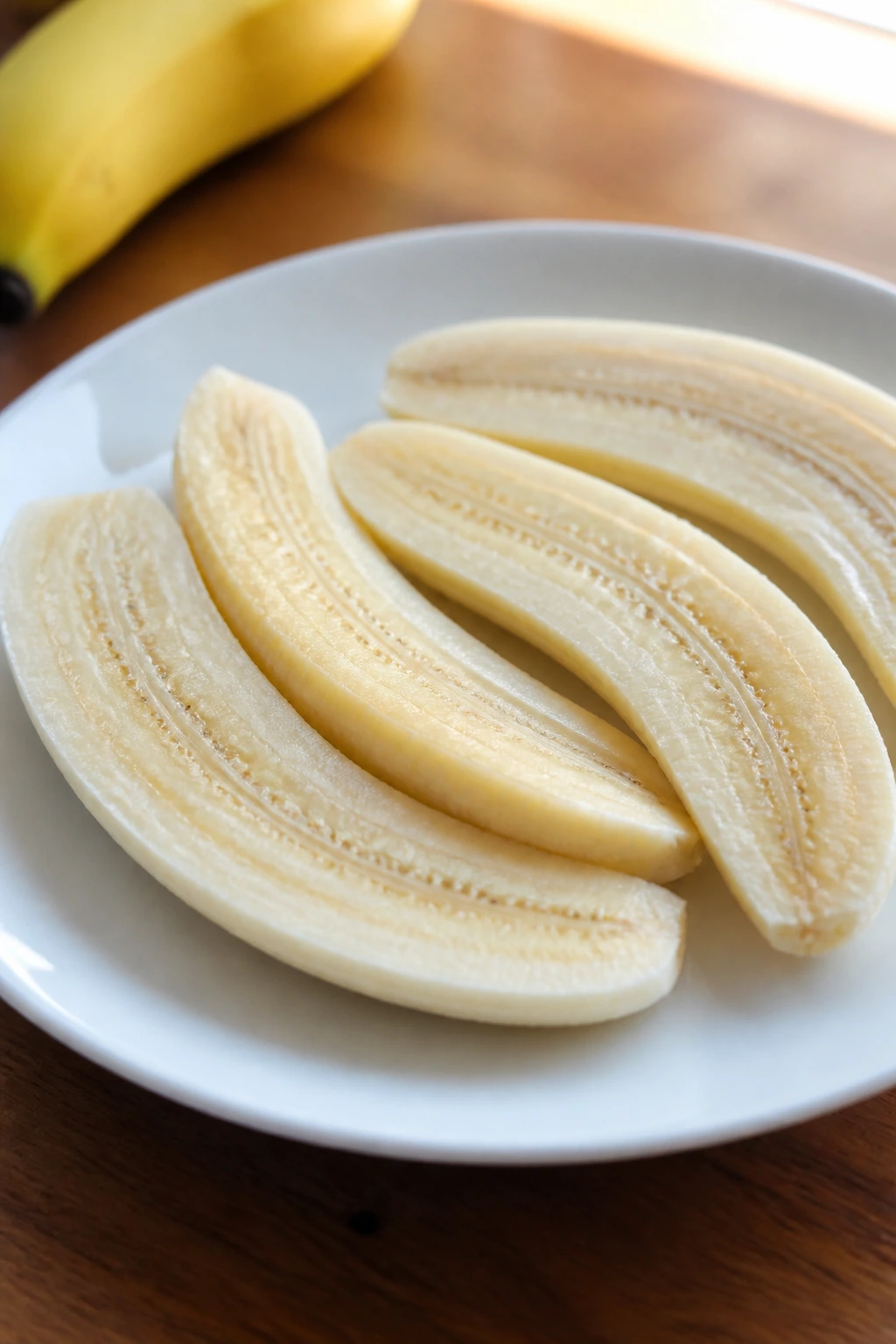 Can You Eat Bananas While Taking Antibiotics? 3 Peeled banana halves on a plate in natural light.