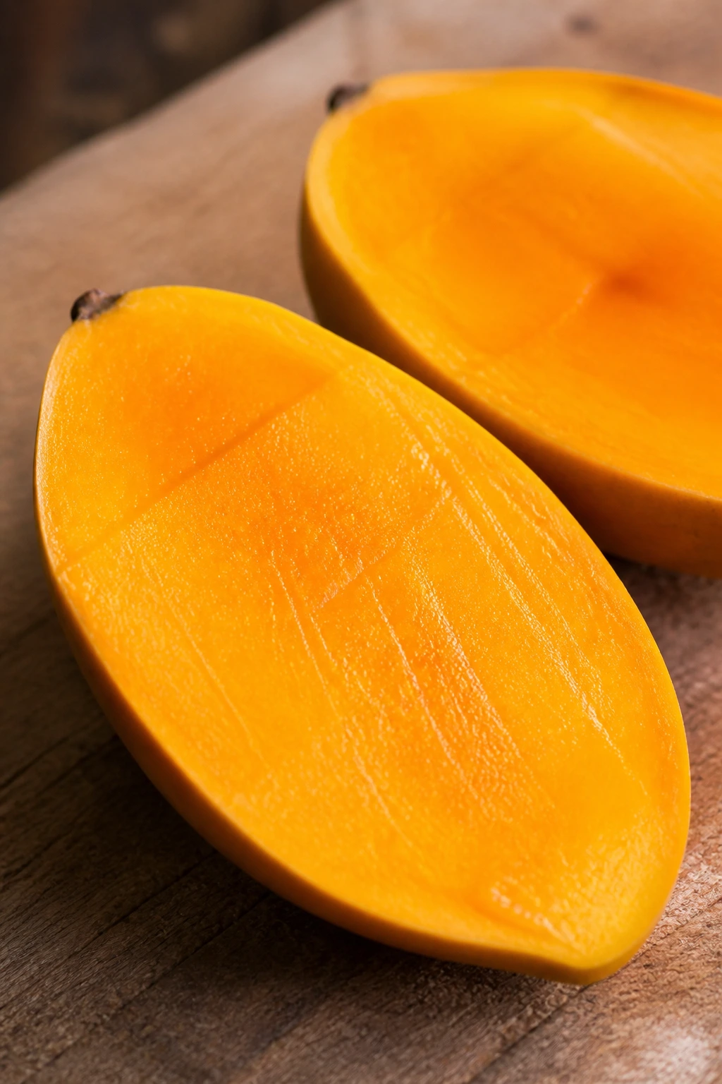 Halved Carabao mango on a wooden board with vivid flesh