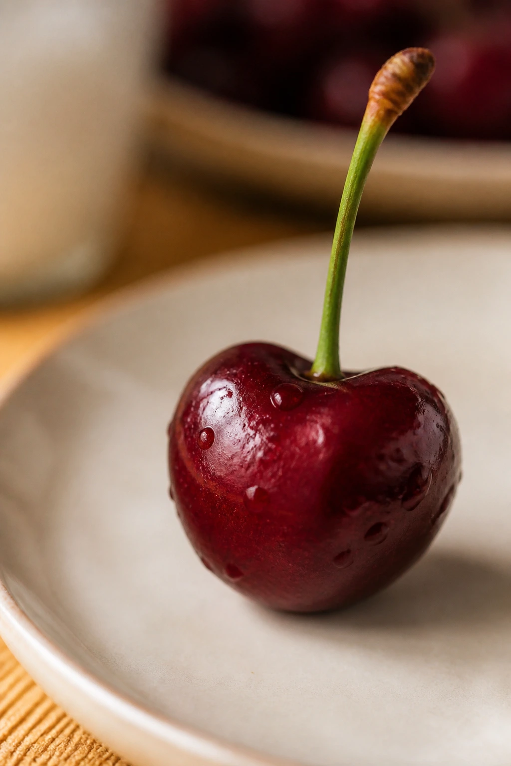 Close-up of a single cherry on a neutral plate in warm kitchen lighting