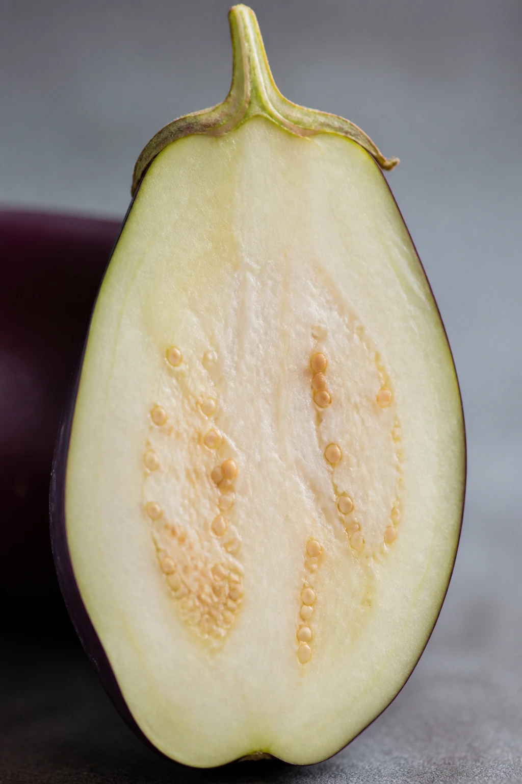 12 Surprising Health Benefits of Garden Egg Fruit 3 Vertical close-up of an eggplant half showing purple skin and pale flesh, filling the frame.