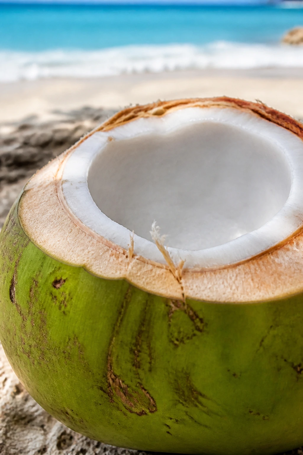 Halved green coconut showing white flesh on a beach