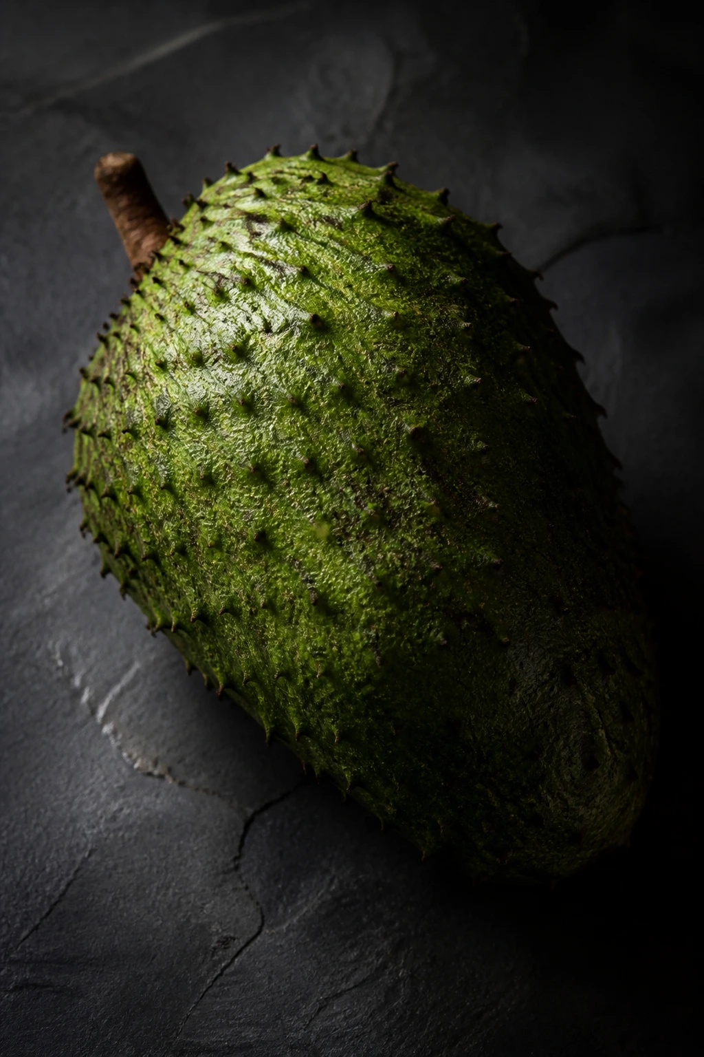 Guanábana fruit with dramatic lighting on a dark surface.