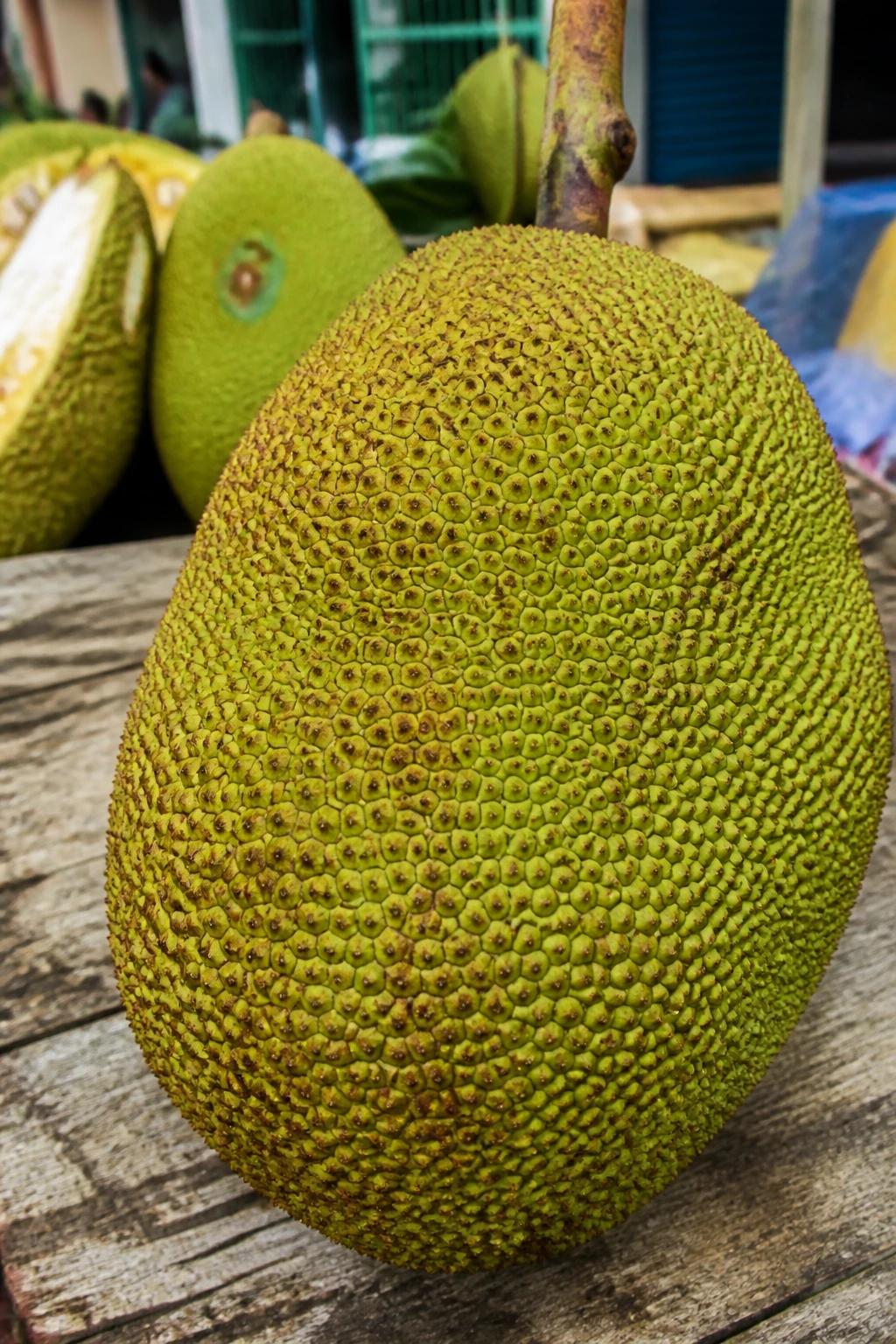 Close-up of ripe jackfruit with textured rind on wooden market table in daylight