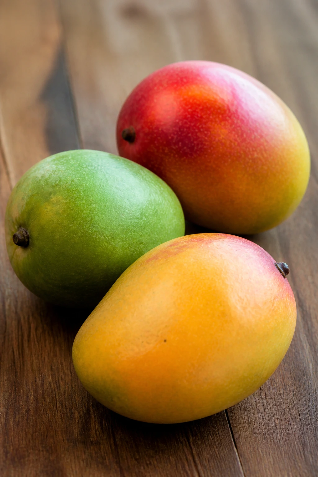 Tropical Showdown: Mango Vs Banana - A Comparison 4 Three mangos with different skin colors on a wooden surface