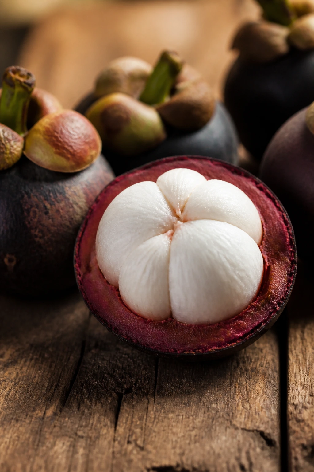 Opened mangosteen with white segments on a wooden surface