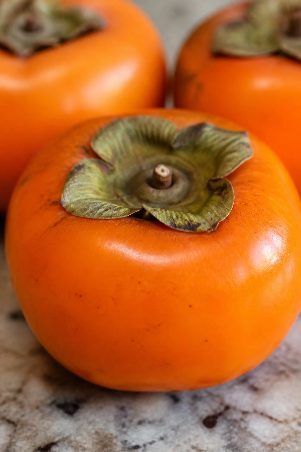 How To Remove Astringency from Persimmon Fruits 2 Close-up of a bright orange persimmon on a neutral kitchen counter
