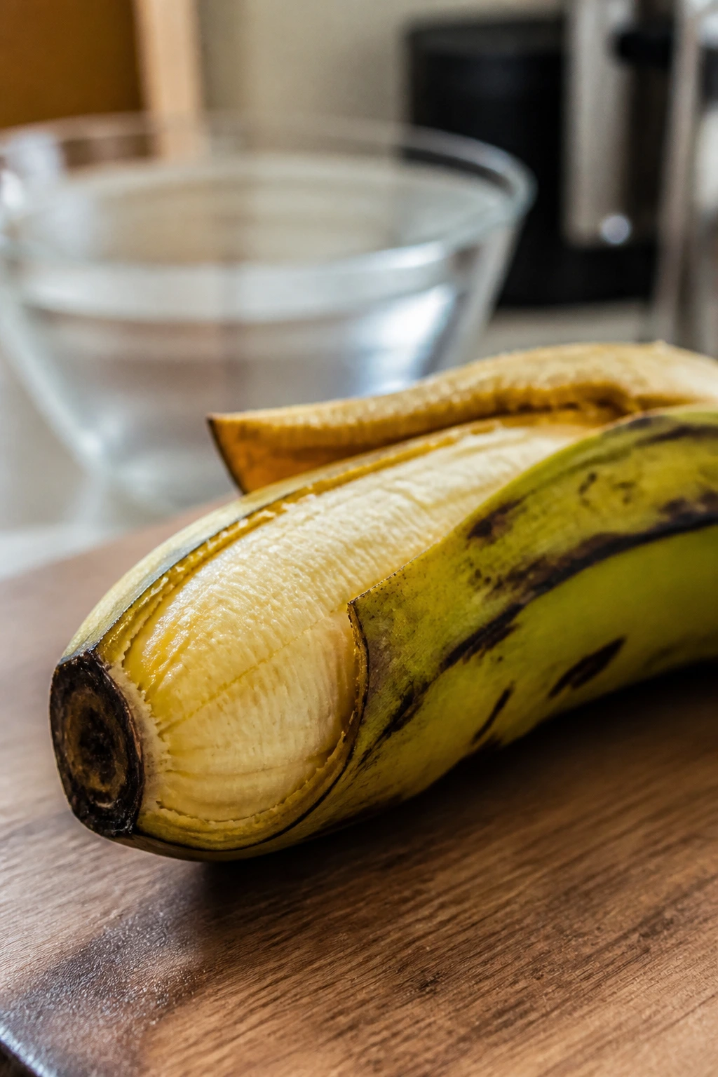Ripe plantain with partially peeled skin near a water bowl in a kitchen