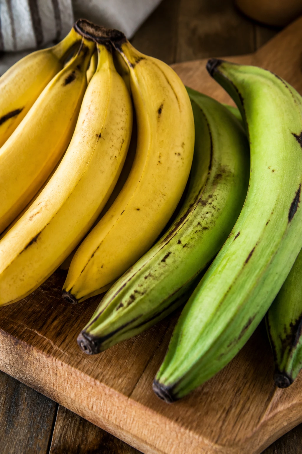 Close-up of bananas and plantains on a wooden cutting board in a kitchen.