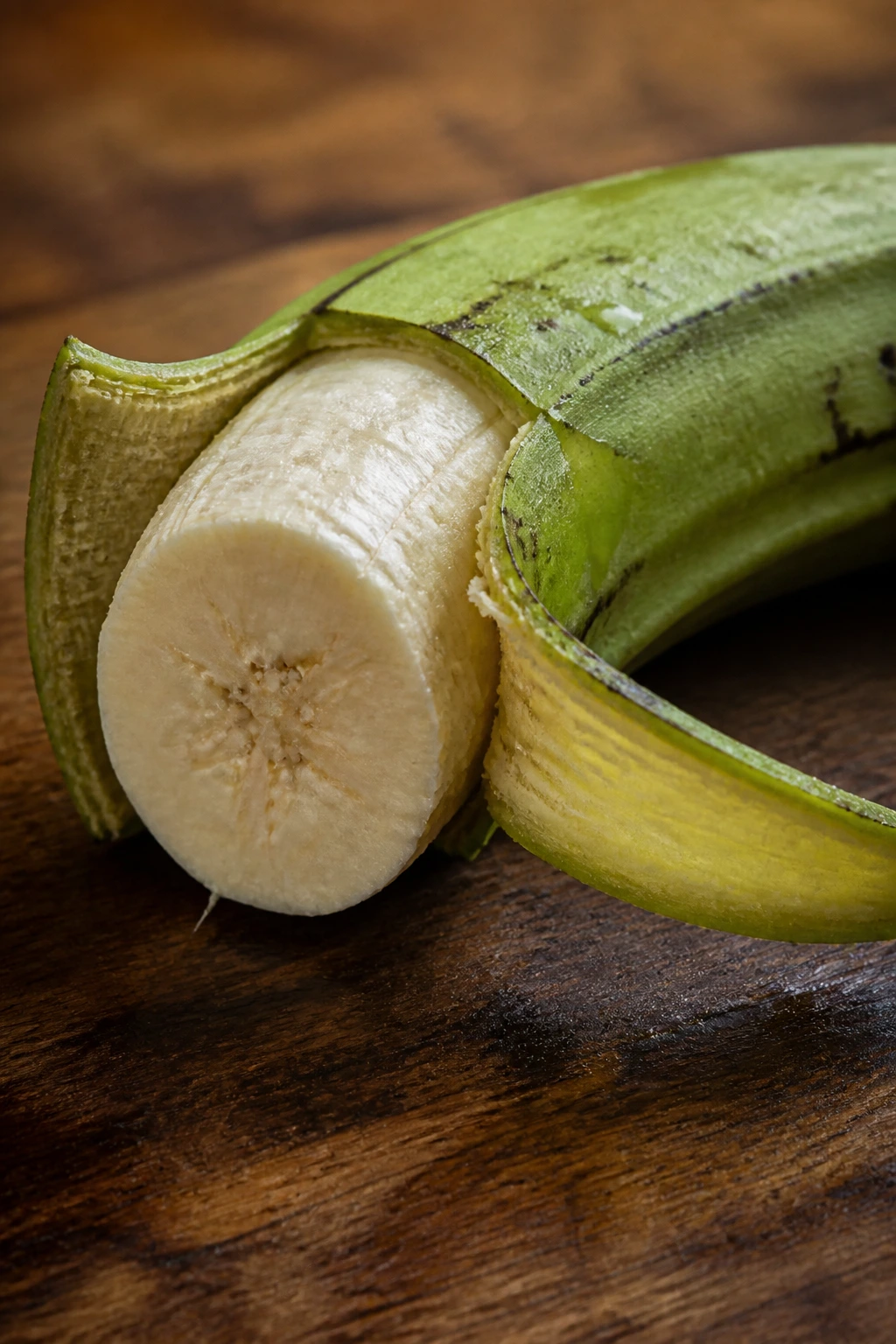Green plantain half-peeled on wooden counter