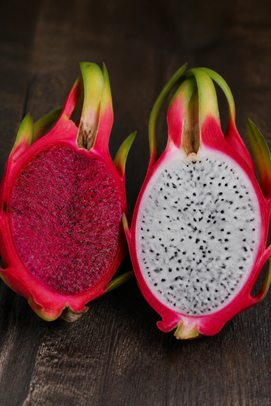 Two dragon fruits, red-fleshed and white-fleshed, on dark wood